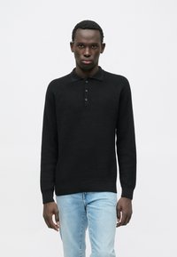Suéter polo de manga comprida preto, em malha, com gola e pala de três botões, combinado com jeans azul claro. Textura suave e corte ajustado.