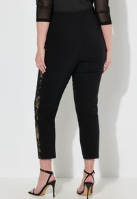Zwarte leggings met een slim fit, met gouden bloemenborduursels langs de zijkanten. Soepele textuur, cropped lengte, gecombineerd met zwarte stilettos.