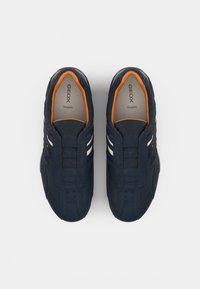 Navy blue sneakers with a textured fabric upper, two white stripes, and an orange-accented inner lining. Features a slip-on design.