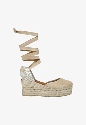 Alpargata cuña beige con suela plataforma trenzada, puntera cerrada y largas cintas para atar alrededor del tobillo en tela beige a juego.