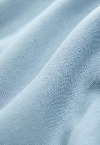 Világoskék pamut anyag sima textúrával, finom kötési mintázattal. Az anyag puha és lágyan hullámosodik.