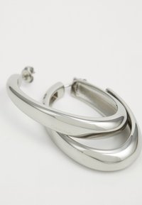 Sølv hoop øreringer med et glat, buet design som har en poleret finish. Graveret med "Calvin Klein" på den ene side.