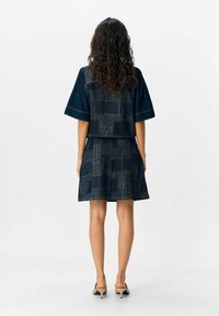 Ensemble en denim avec un haut à manches courtes et une jupe ajustée, tous deux en bleu foncé avec des motifs linéaires texturés et des détails de couture.