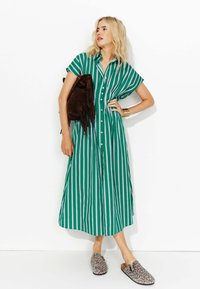 Robe midi rayée verte et blanche, à manches courtes, avec boutonnage à l'avant. Accompagnée d'un sac à franges marron et de chaussures à enfiler imprimé léopard.