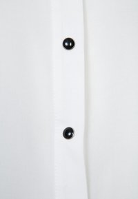 Bílá látka s vertikálním řádkem knoflíků, obsahující dva kulaté černé knoflíky se stříbrnými okraji.