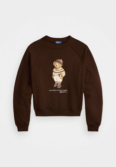 Brūns džemperis ar apaļu kaklu un raglāna piedurknēm, ar grafiku, kurā attēlots lācis ziemas apģērbā un uzraksts "POLO BEAR by RALPH LAUREN."