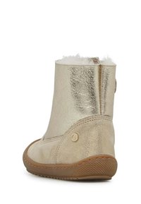 Stivale alla caviglia in metallo dorato con rivestimento in pelliccia sintetica, superficie testurizzata, punta arrotondata e suola in gomma. Dettaglio con bottone laterale vicino alla caviglia.