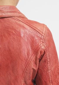 Red leather jacket with a textured surface and perforated details on the shoulders. Features noticeable stitching and a classic collar design.