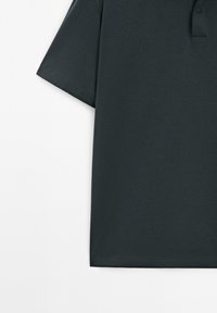 Polo manches courtes vert foncé avec une patte de boutonnage à trois boutons sur fond blanc, montrant la partie supérieure du torse.