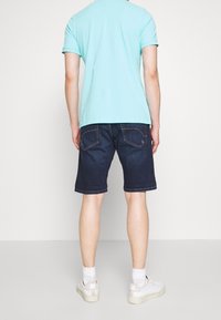 T-shirt bleu à manches courtes, associé à un short en denim foncé. Des baskets blanches et des chaussettes blanches mi-mollet sont portées. Design simple dans l'ensemble.
