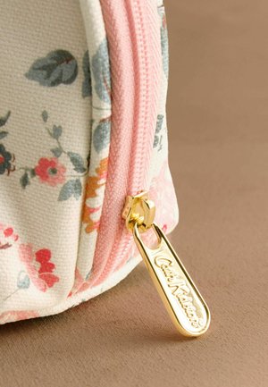 Artimųjų planas gėlėto audinio maišelio su rožine užtrauktuku ir auksiniu užtrauktuko traukikliu, ant kurio išgraviruotas užrašas „Cath Kidston“.