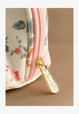 Prim-plan cu un săculeț din material floral, cu un fermoar roz și un pandantiv de fermoar auriu gravat cu inscripția „Cath Kidston.”