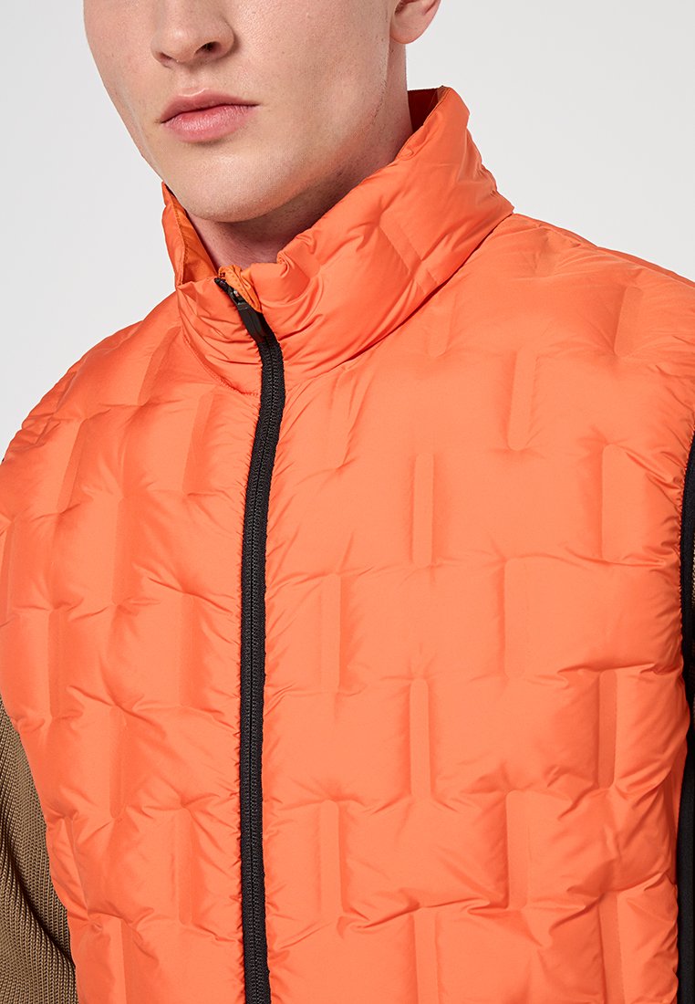 Padded Weste in leuchtendem Orange, mit hohem Kragen, schwarzem Reißverschluss und strukturiertem Steppdesign. Leicht und slim fit.
