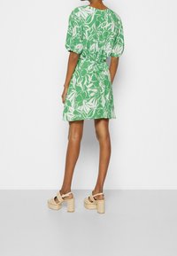 Zelené šaty s květinovým potiskem, krátkými nabíranými rukávy, úzkým pasem a rozšířeným spodním okrajem. Nosené s krémovými sandály na platformě s páskem.