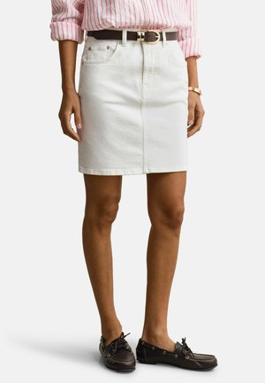 Frau trägt einen weißen Denim-Rock mit Fronttaschen, braunem Gürtel, rosa-weiß gestreiftes Hemd, Goldarmband und dunkelbraune Schnür-Loafer.