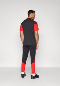 Conjunto atlético preto e vermelho com uma camisa de mangas curtas com detalhes vermelhos e calças combinando com riscas laterais, além de sapatos pretos.