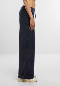Navy blue, wide-leg sweatpants with an elastic waistband, featuring a subtle all-over logo pattern and drawstring detail.