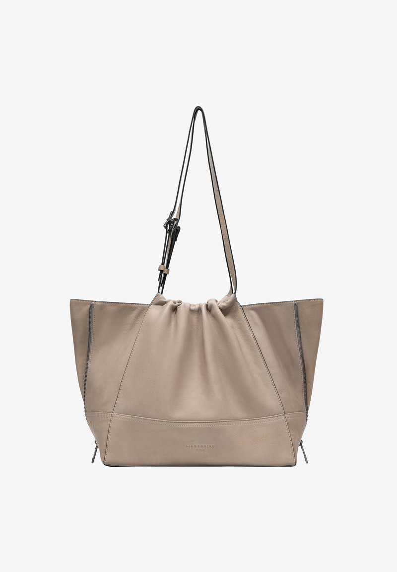 Beige leather tote bag with a slouchy design, drawstring closure, and black accents. Features a zippered side pocket and smooth texture.