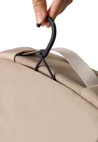 Borsa beige con superficie testurizzata, dotata di un gancio nero e un cordino per l'aggancio. Tracolla visibile sul lato. Dettaglio ravvicinato della ferramenta.