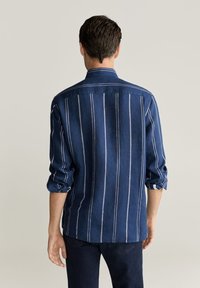 Námořnická modrá pruhovaná košile s límečkem, zahnulanými rukávy a bílými vertikálními pruhy. Vyrobena z měkkého, strukturovaného materiálu.