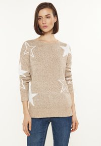 Beige kötött pulóver fehér csillagmintákkal, kerek nyakkivágással és hosszú ujjal, laza fazonnal és bordás mandzsettákkal.