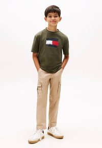 Green short-sleeve t-shirt with a red, white, and blue logo; beige cargo pants with pockets; white sneakers with a tan sole.
