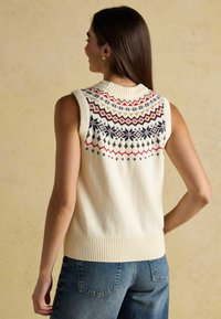 Bez piedurknēm krēmbalts adīts džemperis ar rakstainu joku sarkanā, zilā un brūnā krāsā. Džemperim ir ribota apkakle un mala ar taisnu griezumu.