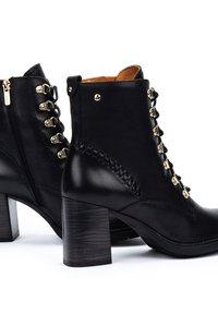 Botines de cuero negro hasta el tobillo con cremallera lateral, acentos de ojales dorados, un tacón texturizado y detalles trenzados a lo largo de las costuras.