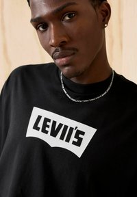 T-shirt en coton noir avec un grand logo blanc de Levi's à l'avant. Le tissu semble lisse avec une coupe décontractée et des manches courtes.