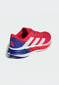 Roter Laufschuh mit strukturiertem Mesh-Obermaterial, weißen drei Streifen, einem Farbverlauf zu Blau an der Ferse und einer weißen Sohle mit roten Akzenten.