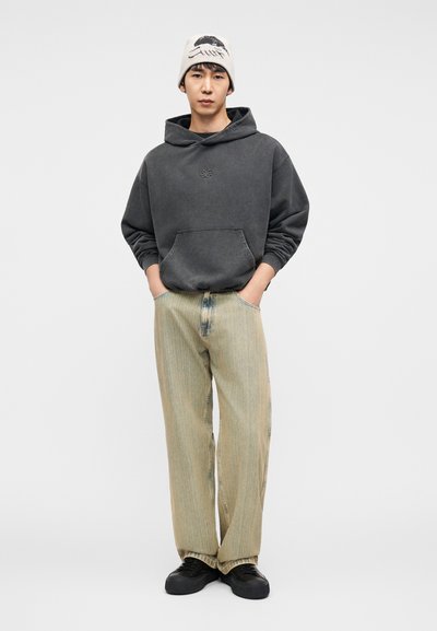 Γκρι φούτερ με φλις ύφασμα και τσέπη καγκουρό· ανοιχτόχρωμα τζιν με ίσια γραμμή· μαύρα αθλητικά παπούτσια· λευκό σκουφάκι με γραφικό σχέδιο.