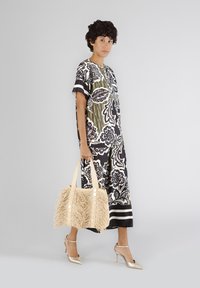 Floral-patterned black and white dress with green accents, paired with a cream fringed bag and metallic heels. Smooth fabric and relaxed fit.
