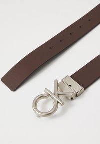 Brown leather belt featuring a metallic buckle with a circular design and embossed lettering, single prong and five adjustable holes.