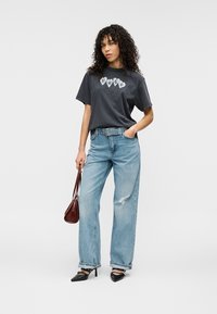 Γκρι βαμβακερό t-shirt με γραφικό «HUGO», συνδυασμένο με ανοιχτό μπλε ψηλόμεσο τζιν με σκισίματα. Συμπληρώνεται με καφέ τσάντα και μαύρες γόβες.