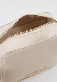 Kosmetická taška Valentino z béžové kůže s texturovaným povrchem, zlatým zipem a vyraženým logem. Kompaktní pravoúhlý design.