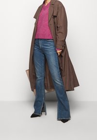 Brun rutig trenchcoat, rosa v-ringad tröja och utsvängda blå jeans med sprund. Djärva, kontrasterande färger och varierande texturer ingår.