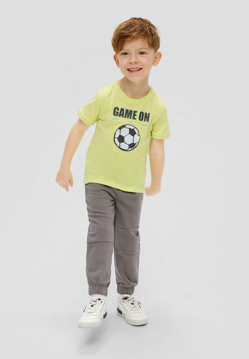 Groene t-shirt met "GAME ON" print en voetbal graphic, gecombineerd met grijze joggingbroek en witte sneakers, met elastische manchetten.