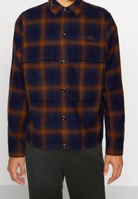 Rutig flanellskjorta med marinblå och orange färger, knappstängning, två bröstfickor och krage. Mjuk textur.