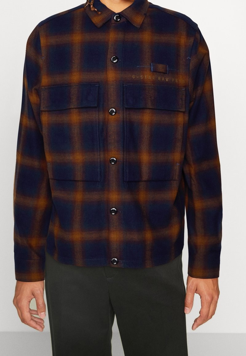 Rutig flanellskjorta med marinblå och orange färger, knappstängning, två bröstfickor och krage. Mjuk textur.