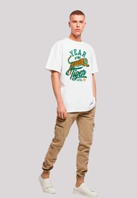 White cotton t-shirt featuring a colorful "Year of the Tiger" graphic, paired with beige cargo pants and white sneakers.
