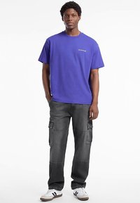 Violeta kokvilnas T-krekls ar apaļu kakla izgriezumu un īsām piedurknēm, kombinēts ar melnām cargo biksēm ar vairākiem kabatām un brīva piegriezuma.