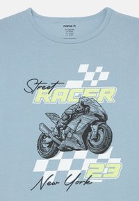 Lys blå bomulls-t-skjorte med svart motorsykkelgrafikk og teksten "Street RACER New York 23" med rutete mønster som aksent.