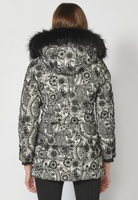 Melnā un baltā paisley rakstā izšūts mētelis ar melnu mākslīgo kažokādu kapuci un elastīgām piedurknēm. Dizainā iekļautas sarežģītas ziedu detaļas.