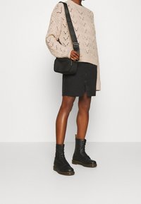 Gebreide crèmekleurige trui met een patroon, gecombineerd met een zwarte denim rok met een frontsplit. Zwarte veterlaarzen in combatstijl. Kleine zwarte tas.