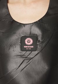 Melns, teksturēts audums ar izteiktām krokām; iekļauts kvadrātveida laukums ar rozā grafiku un tekstu: "VENUS IN BLACK NEW YORK."