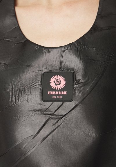 Black, textured fabric with prominent creases; features a square patch with pink graphic and text: "VENUS IN BLACK NEW YORK."
