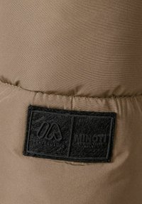 Beige tyg med en slät textur som har en svart filtetikett. Etiketten visar "MINOTI" och "PERFORMANCE" i fet, texturerad stil.