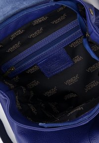 Wnętrze niebieskiej skórzanej torby na ramię z kieszenią na suwak. Podszewka pokazuje powtarzający się wzór logo "VENEZIA" na czarnym tle.