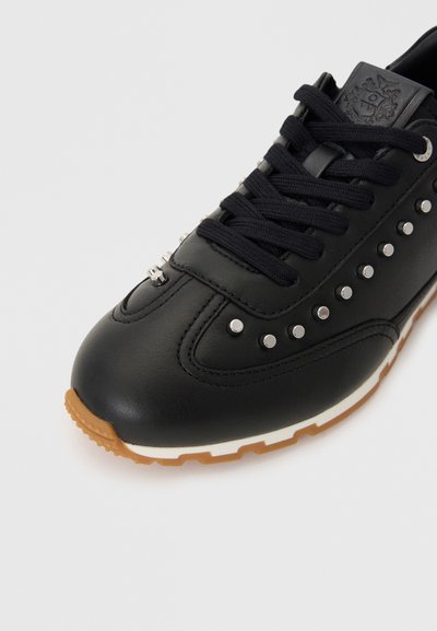 Zwarte leren sneaker met zilveren studs langs de zijkant, zwarte veters en een gumrubberen zool. Heeft een logo op de tong.