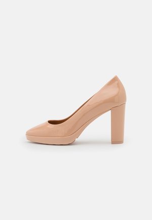 Zapato de tacón alto de charol beige con puntera redondeada y tacón bloque, mostrado sobre un fondo blanco liso.